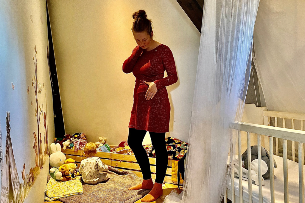 Women looking at her body after baby in red dress with baby's room in background