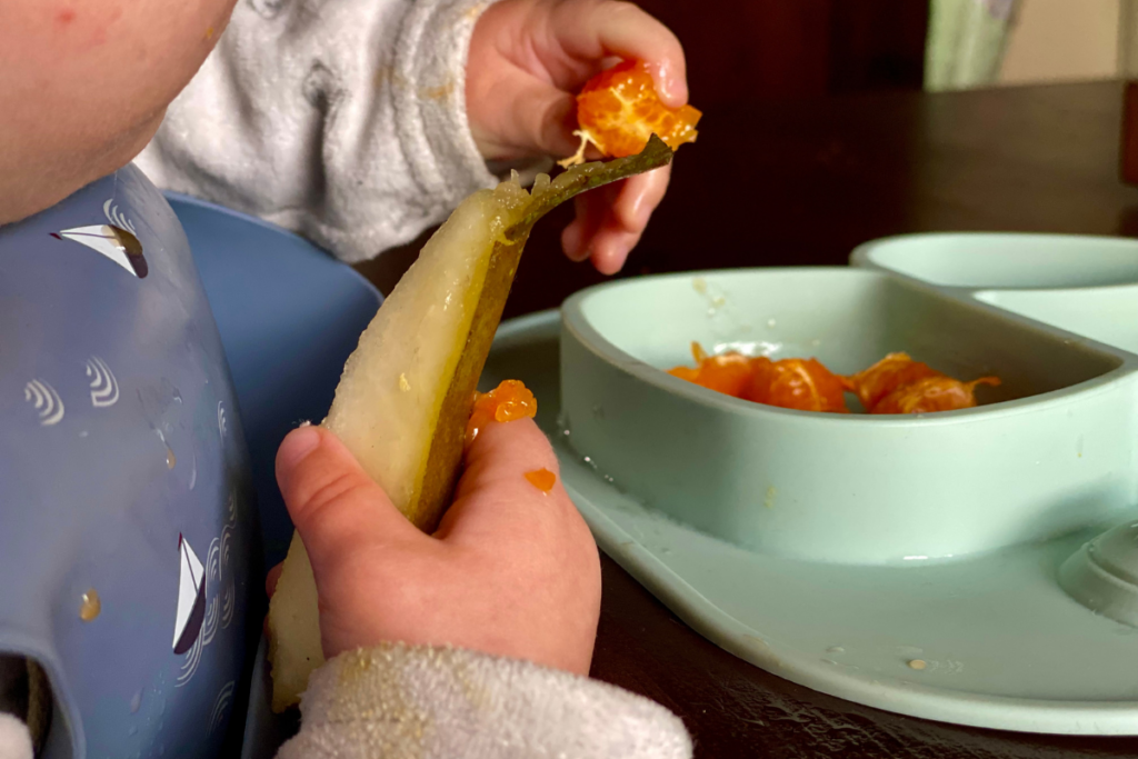 close up of baby hands eating mandarine and pear