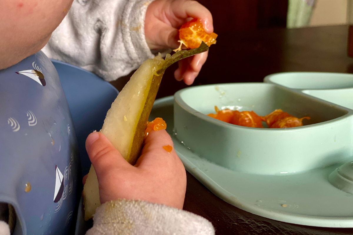 close up of baby hands eating mandarine and pear