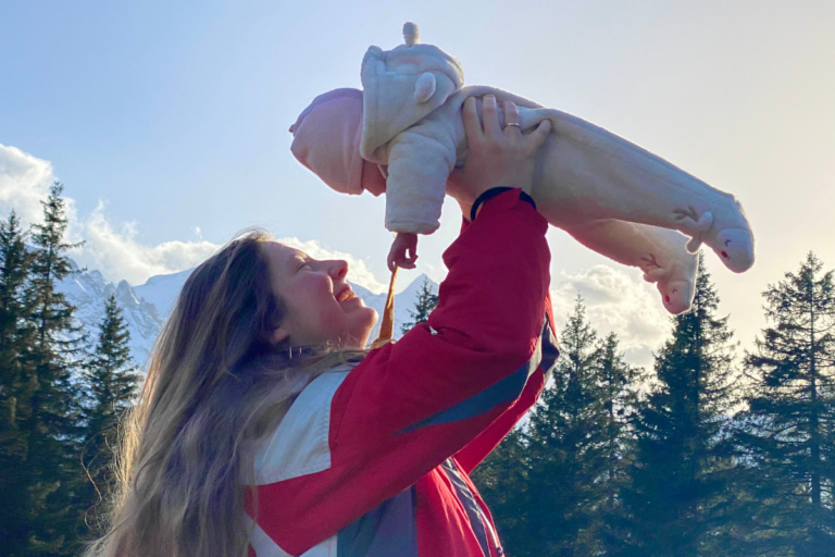 New mom holding little baby in the air with mountains in the background