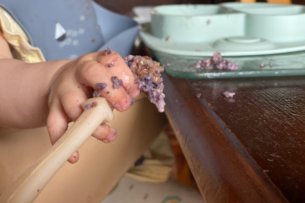 baby holding a spoon with oat meal weaning with combined approach 