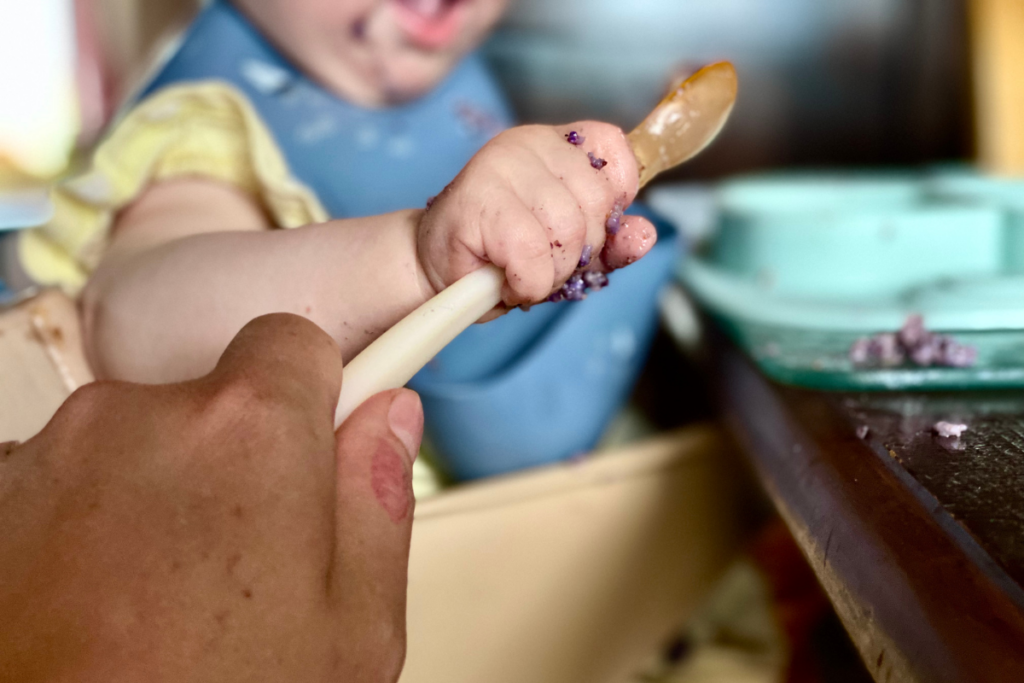 baby and adult hand holding spoon