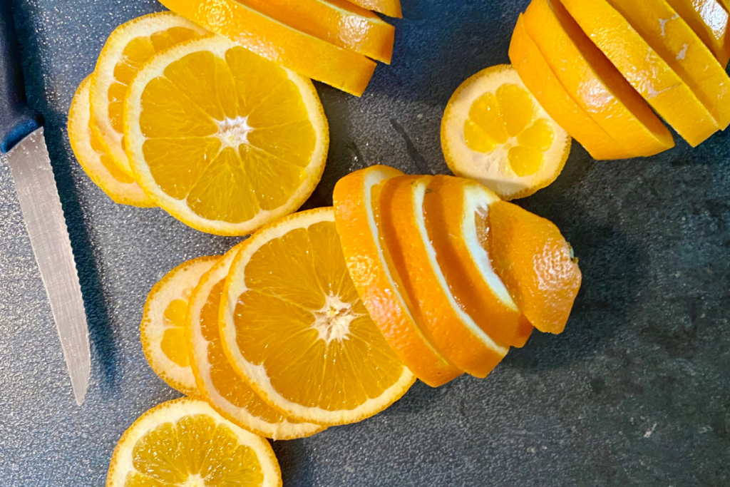 slices oranges with knife on glass cutting board