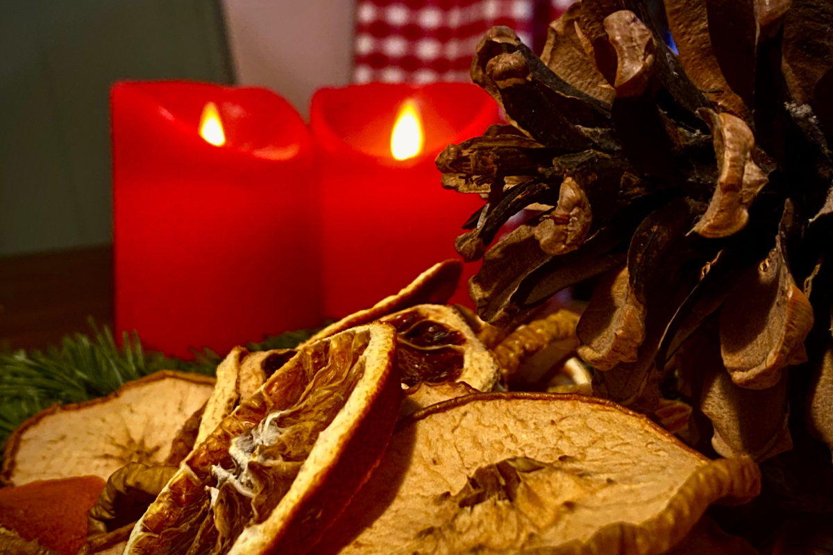 Simple natural christmas decoration pina apple close op with apple and orange slices and two red candles in the back