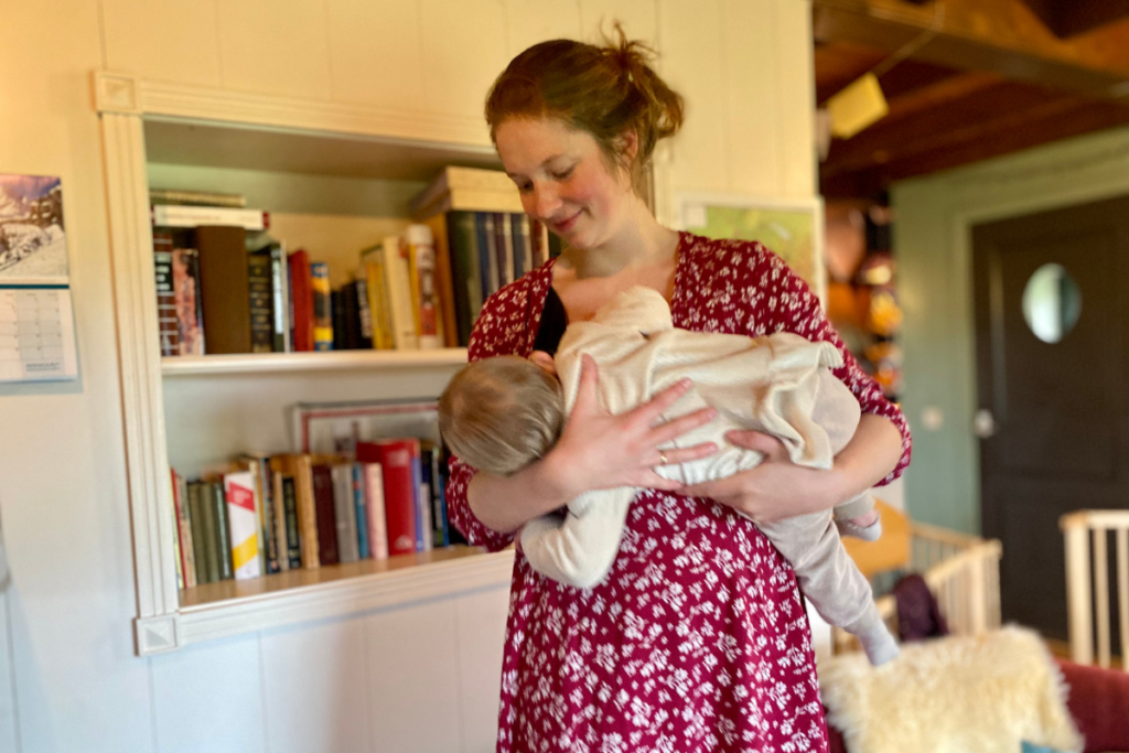 Women breastfeeding discreetly in standing position in front of book shell 