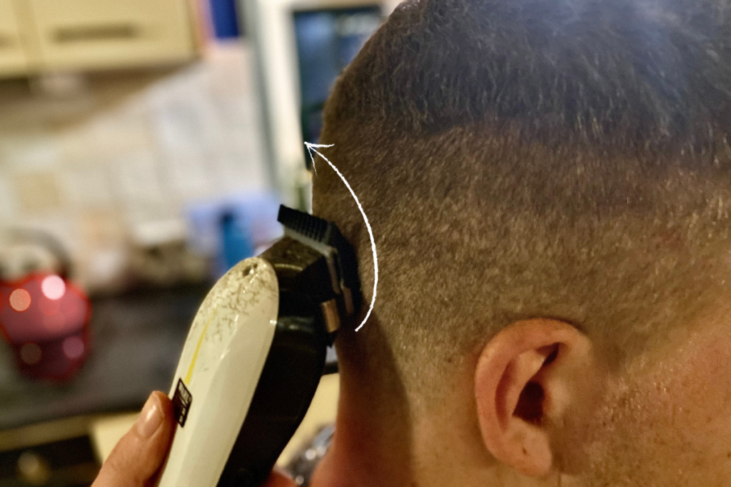 close up of man's head with a hair clipper and a arrow pointing the direction the hair clipper should move