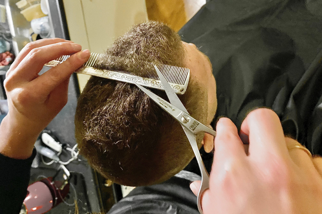 close up form the top of a women cutting the top of a man's hair