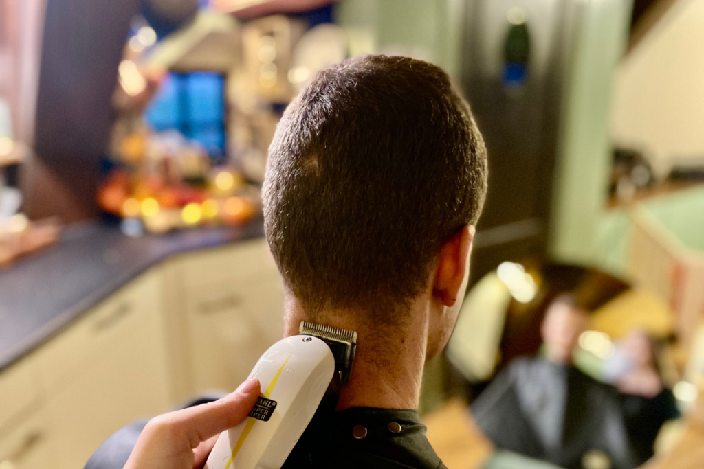 mans head with living space in background and hair clipper at the bottom of head shaving of the hair