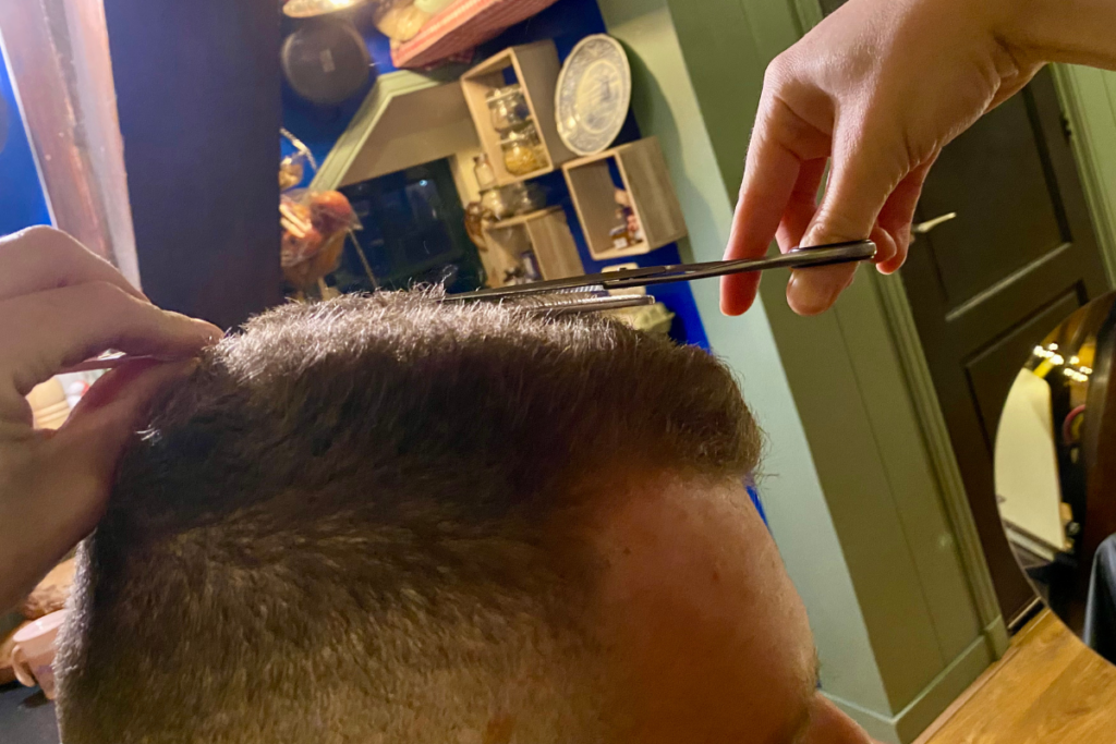 close up form the side of a women cutting the top of a man's hair 