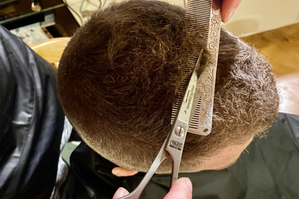 close up form the top of a women cutting the top of a man's hair