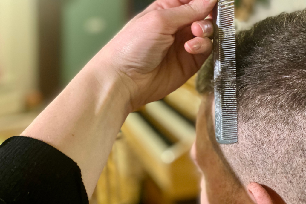 close up from a woman's hand holding a comb up to a man's head combing the hair in a vertical line