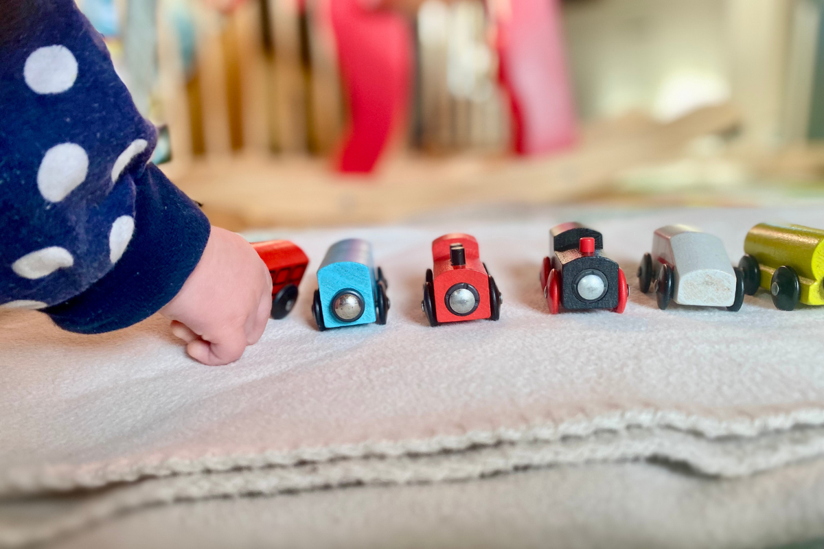 Wooden trains standing in a line and baby grabbing one of them close up