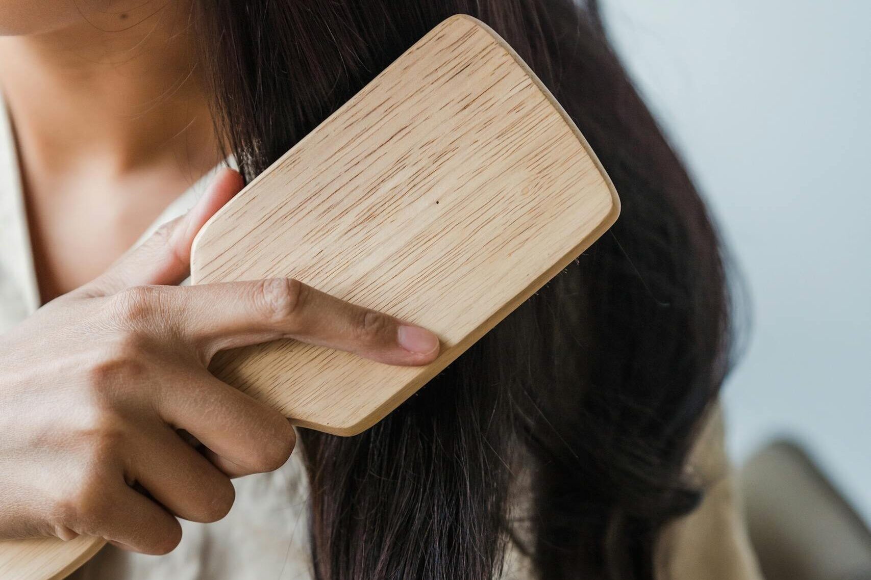 Close-up of a woman brushing her long dark hair with a wooden brush indoors.