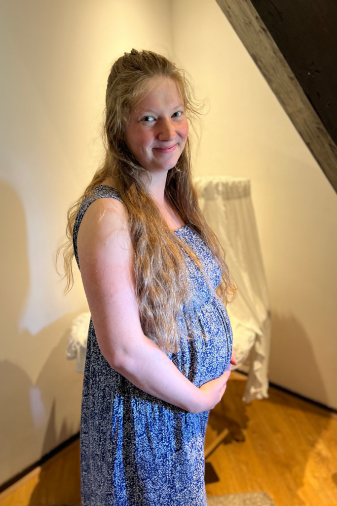 picture of pregnant women smiling in front of a crib in the second trimester