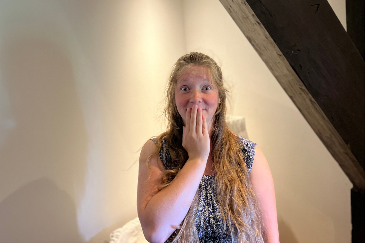 women standing in blue dress standing in front of a crib holding her hand over her mouth in surprise